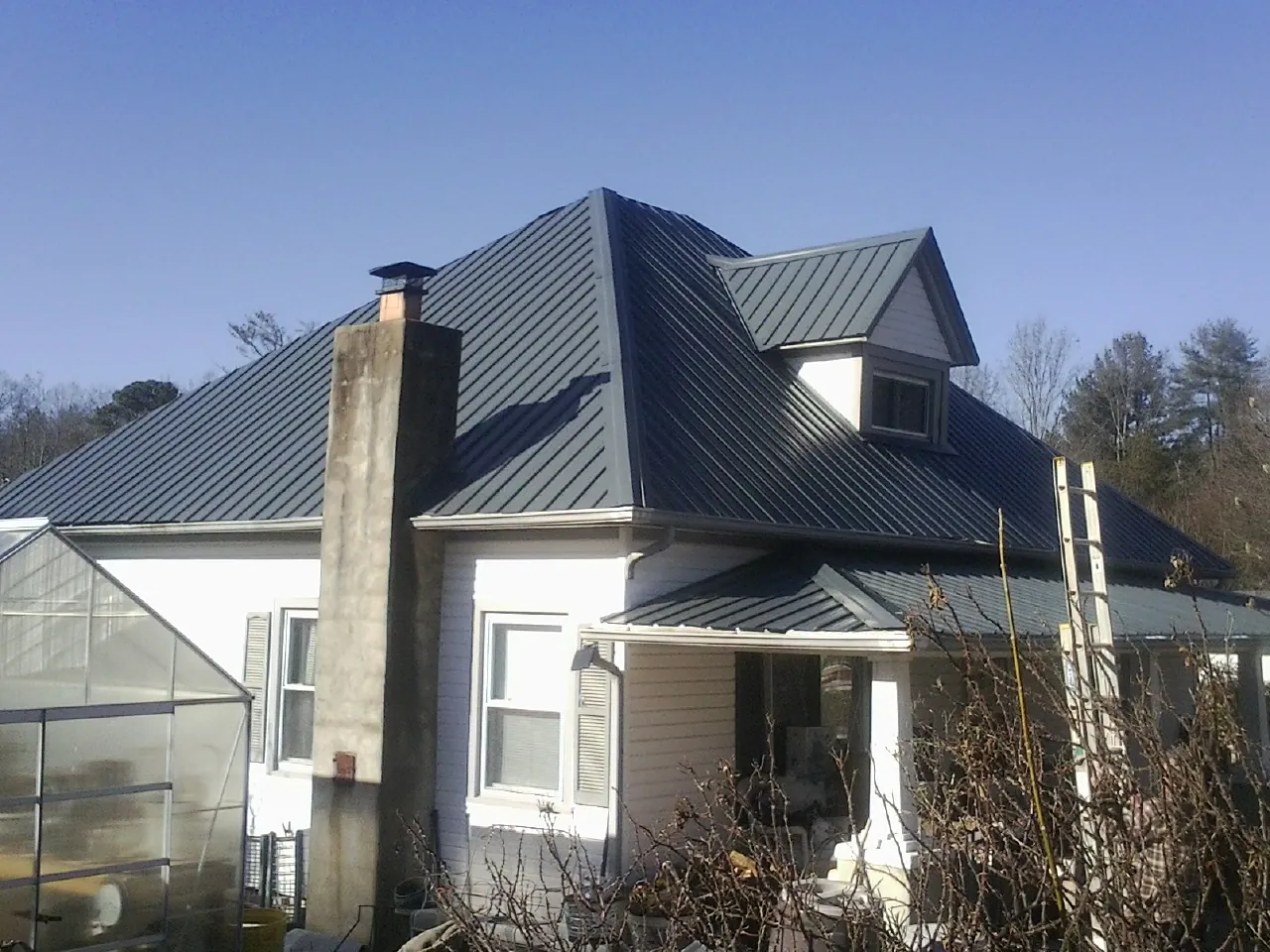 Dark blue standing seam metal roof on a white farmhouse with dormer — Slate & Tile Roof Repair by Roofing Brothers in Vader