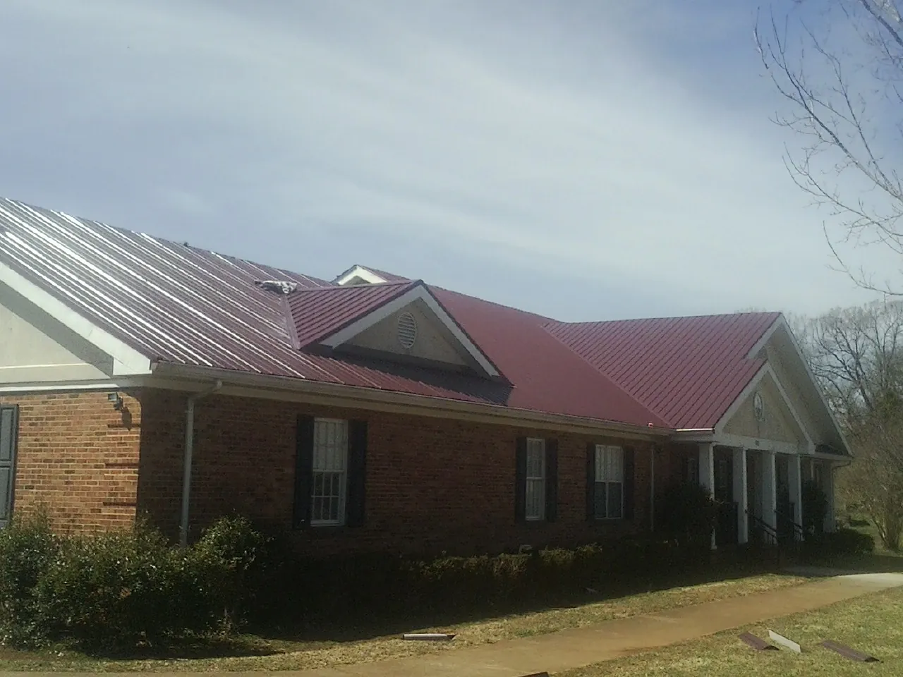 Red metal roof with gabled entries on a long brick building, from a Hail Damage Roof Repair job in Vader