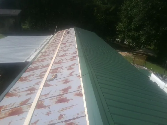 Old rusted panels beside newly installed green metal roofing — Wind Damage Roof Repair by Roofing Brothers in Vader