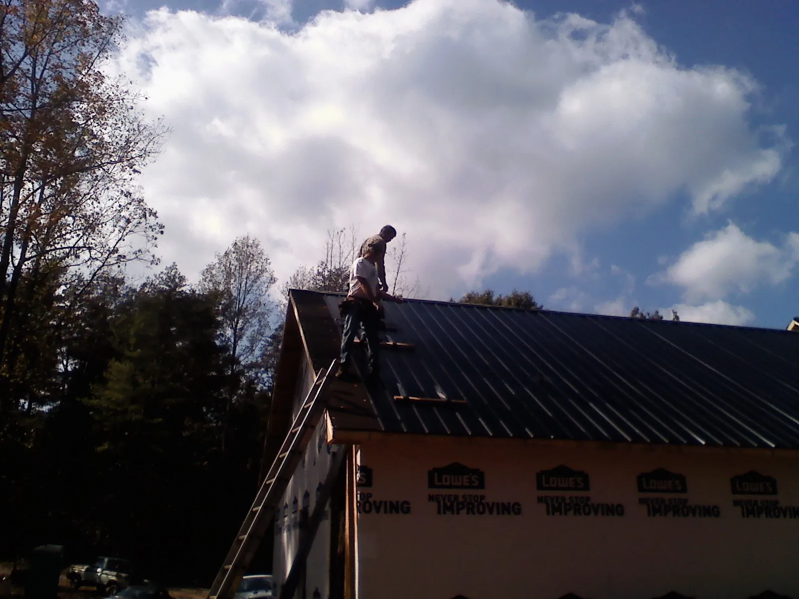 Roofer fastening dark metal panels high against a cloudy sky, from a Roof Inspection job in Vader